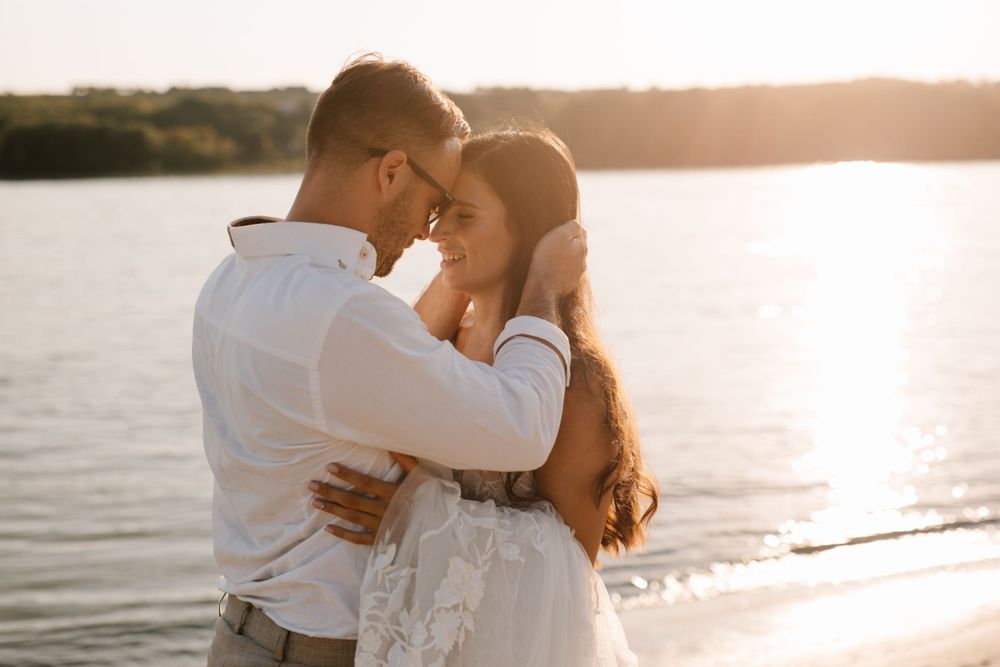 Romantic sunset silhouette of couple embracing by water during golden hour.