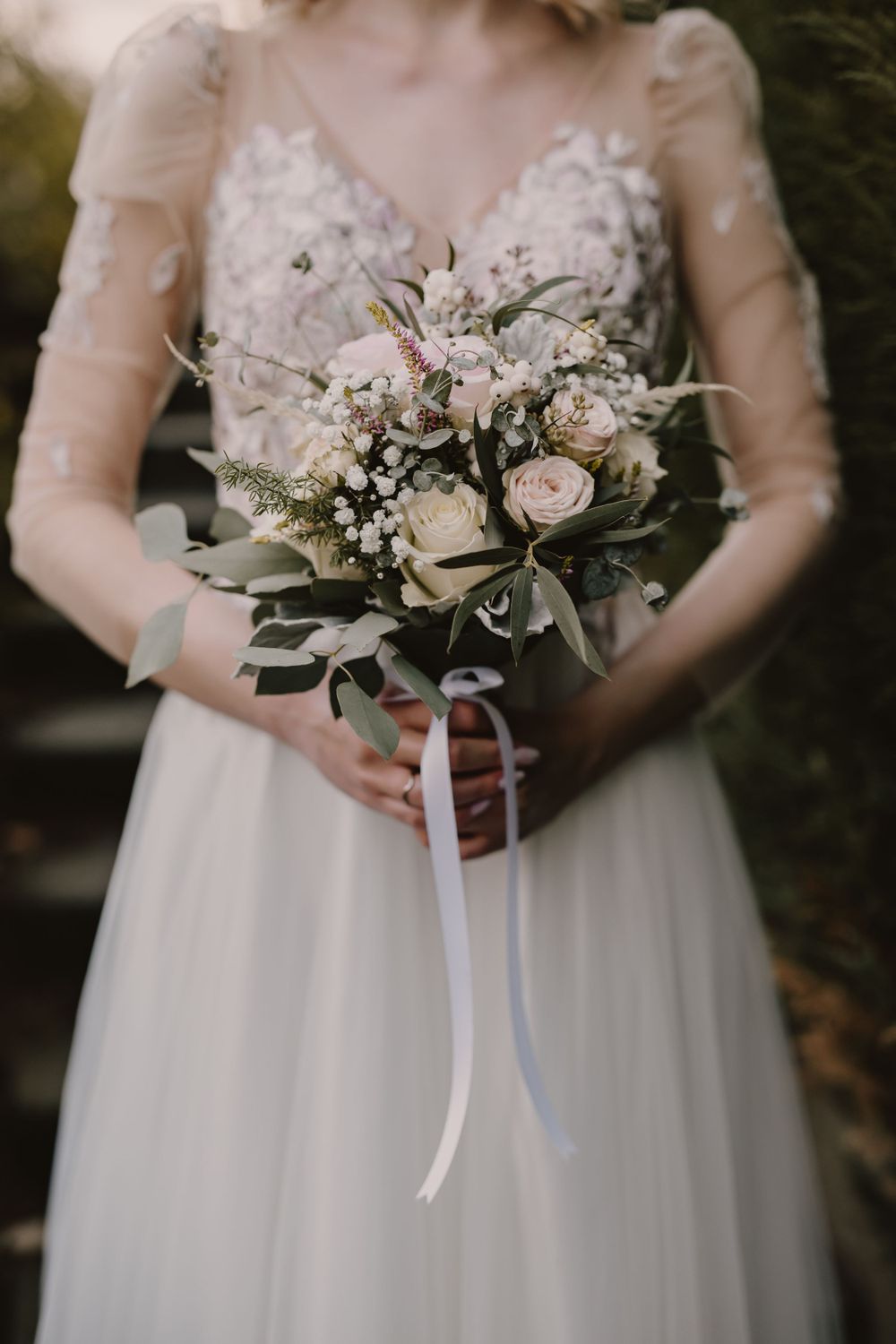 Bride holding a romantic bouquet of white and blush roses with eucalyptus.
