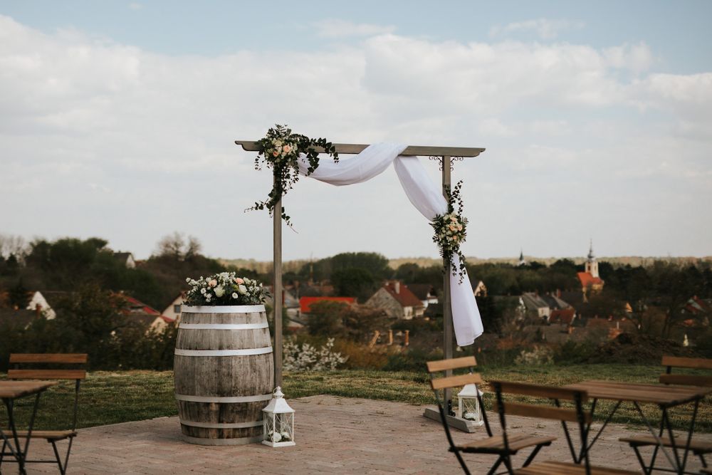 A rustic outdoor wedding ceremony setup with barrel and wooden arch decorated with white fabric.