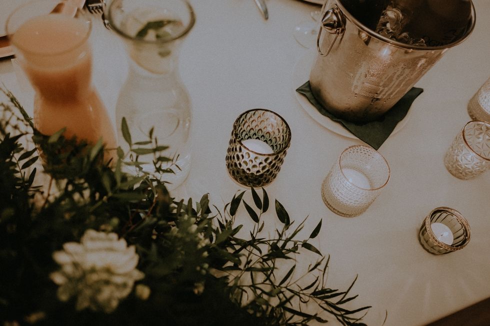 Moody table decor with candles, greenery and champagne bucket in evening lighting.