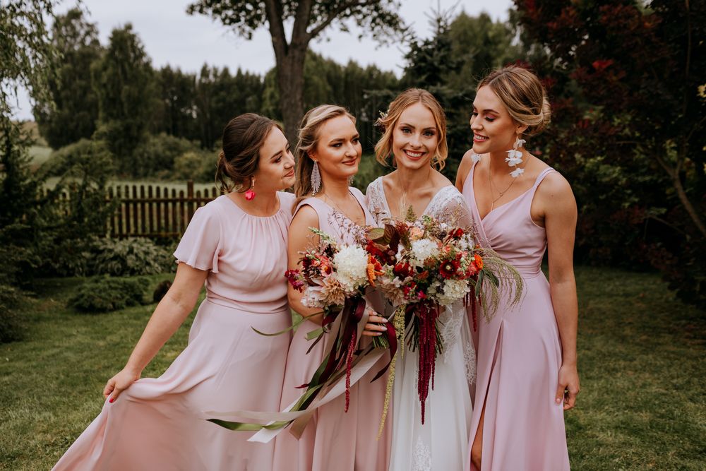 Bridal party in pink dresses holding colorful bouquets while laughing in garden setting.