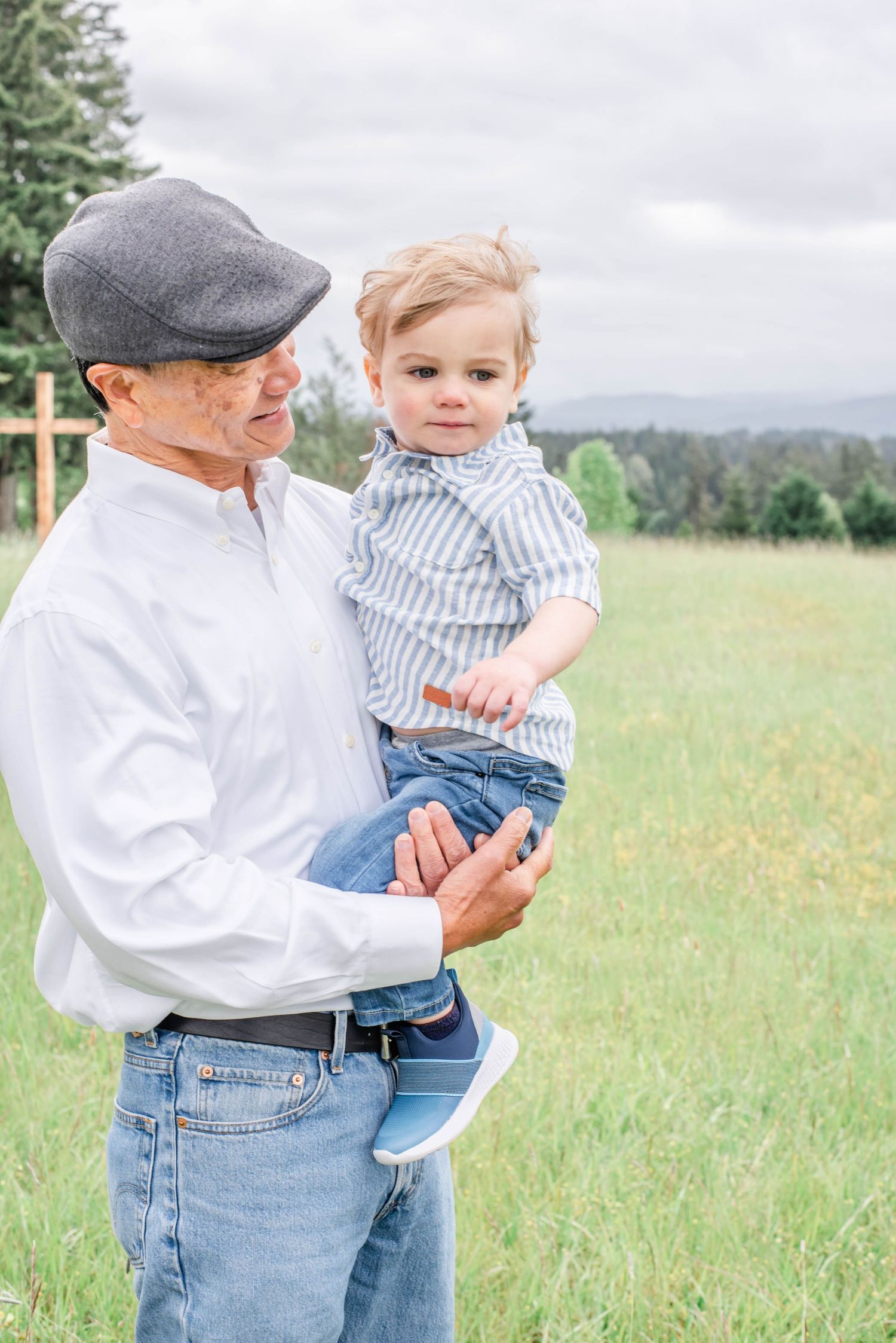 Adult figure in gray cap and white shirt holds small child in striped shirt against scenic mountain backdrop.