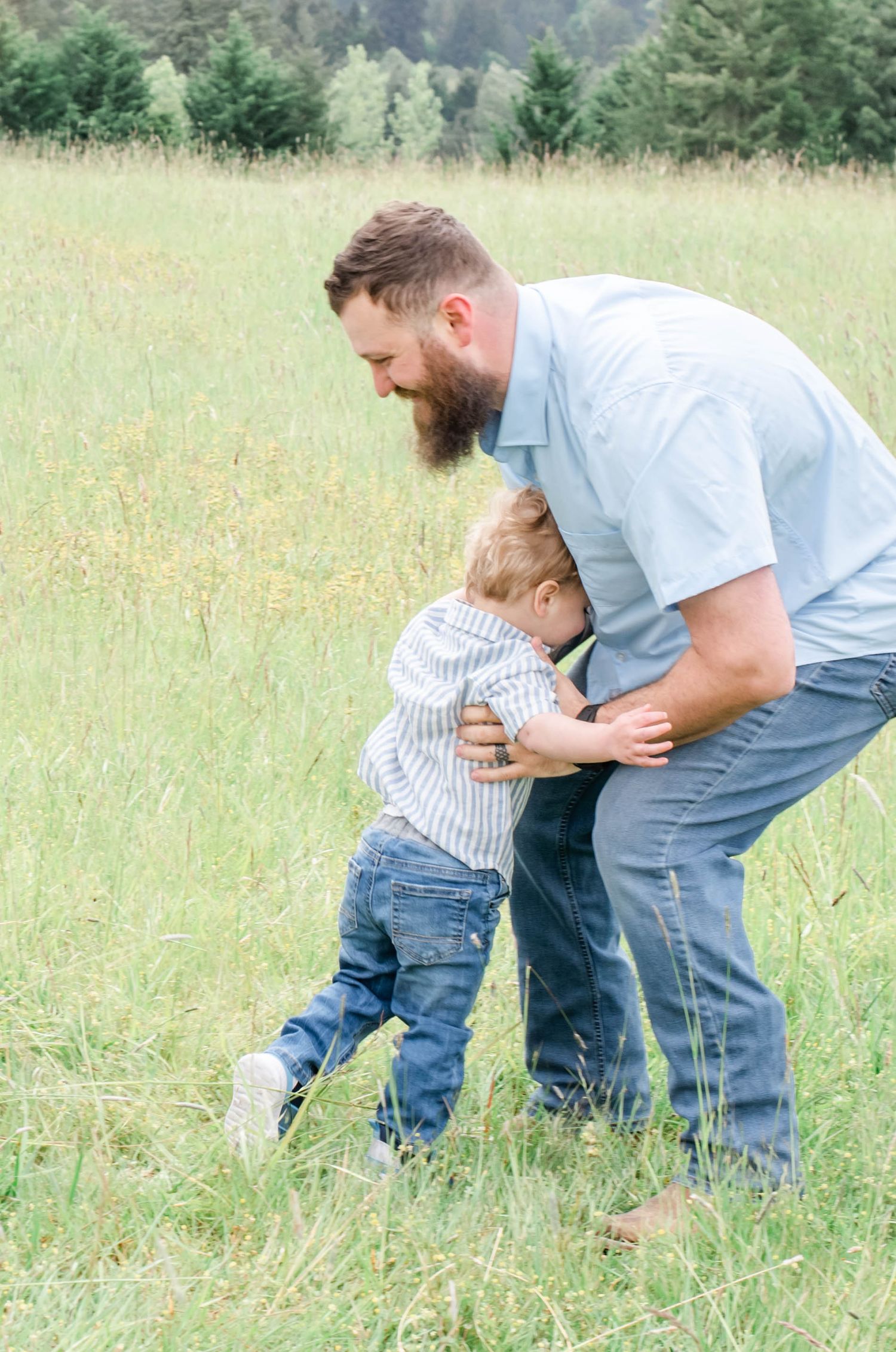 Two people playing and crawling through tall grass in a sunny field with mountains in the distance.