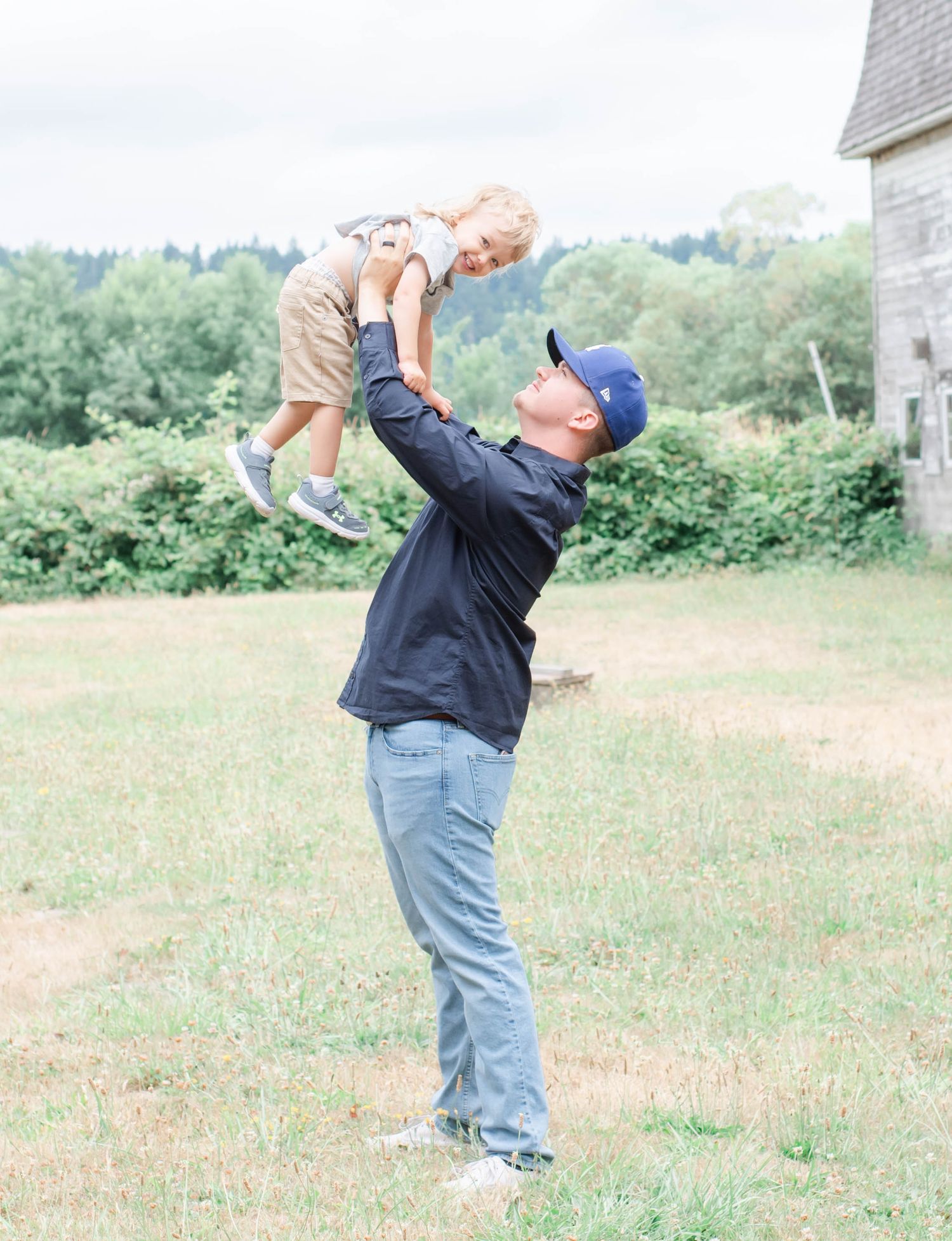 Parent lifts child playfully in air against rural landscape backdrop.