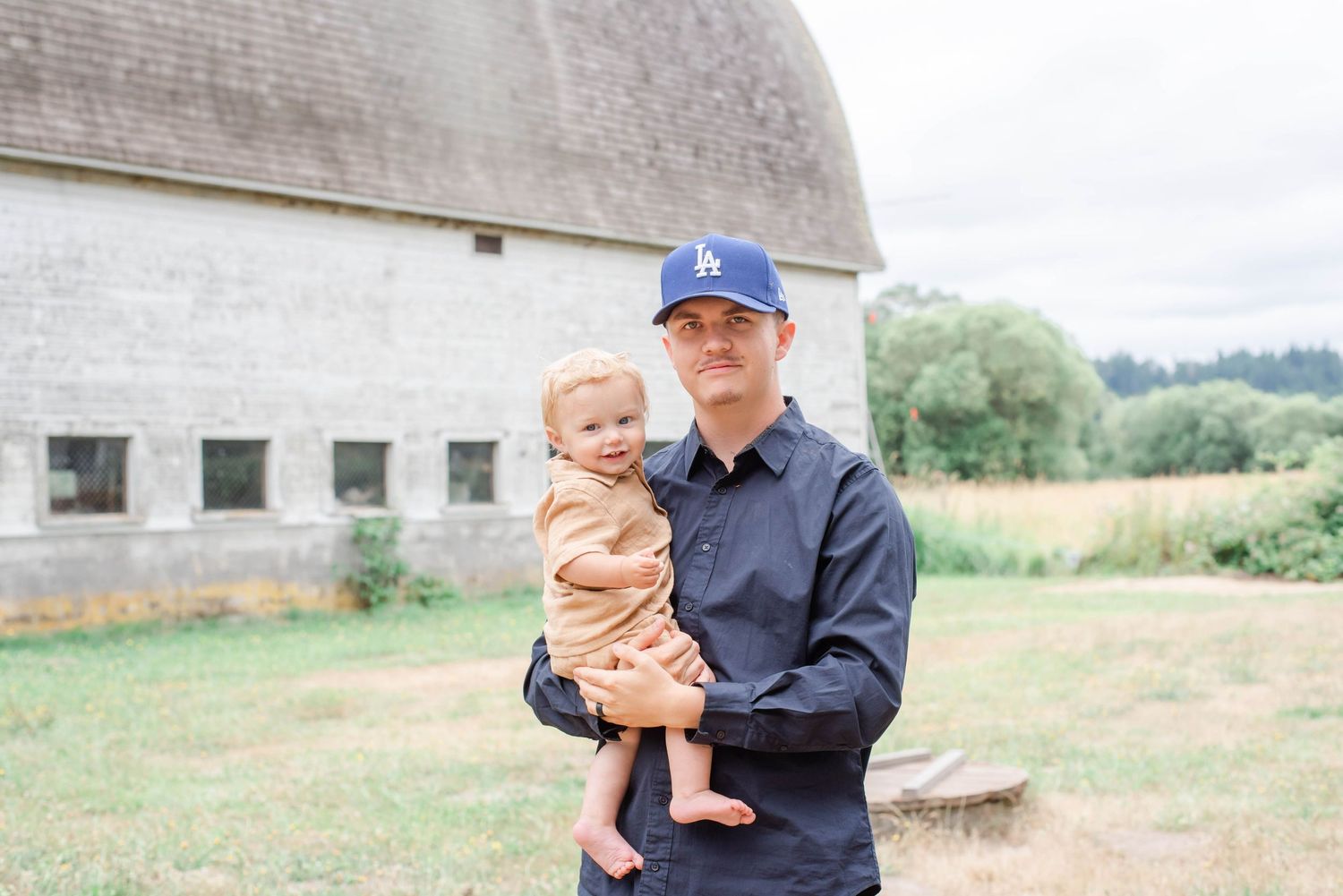 Parent and child share playful moment on grassy field near rustic building.