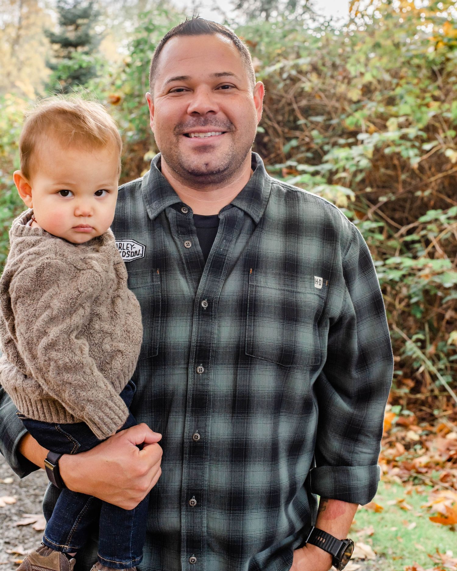 Parent and children pose together outdoors with autumn foliage in background.