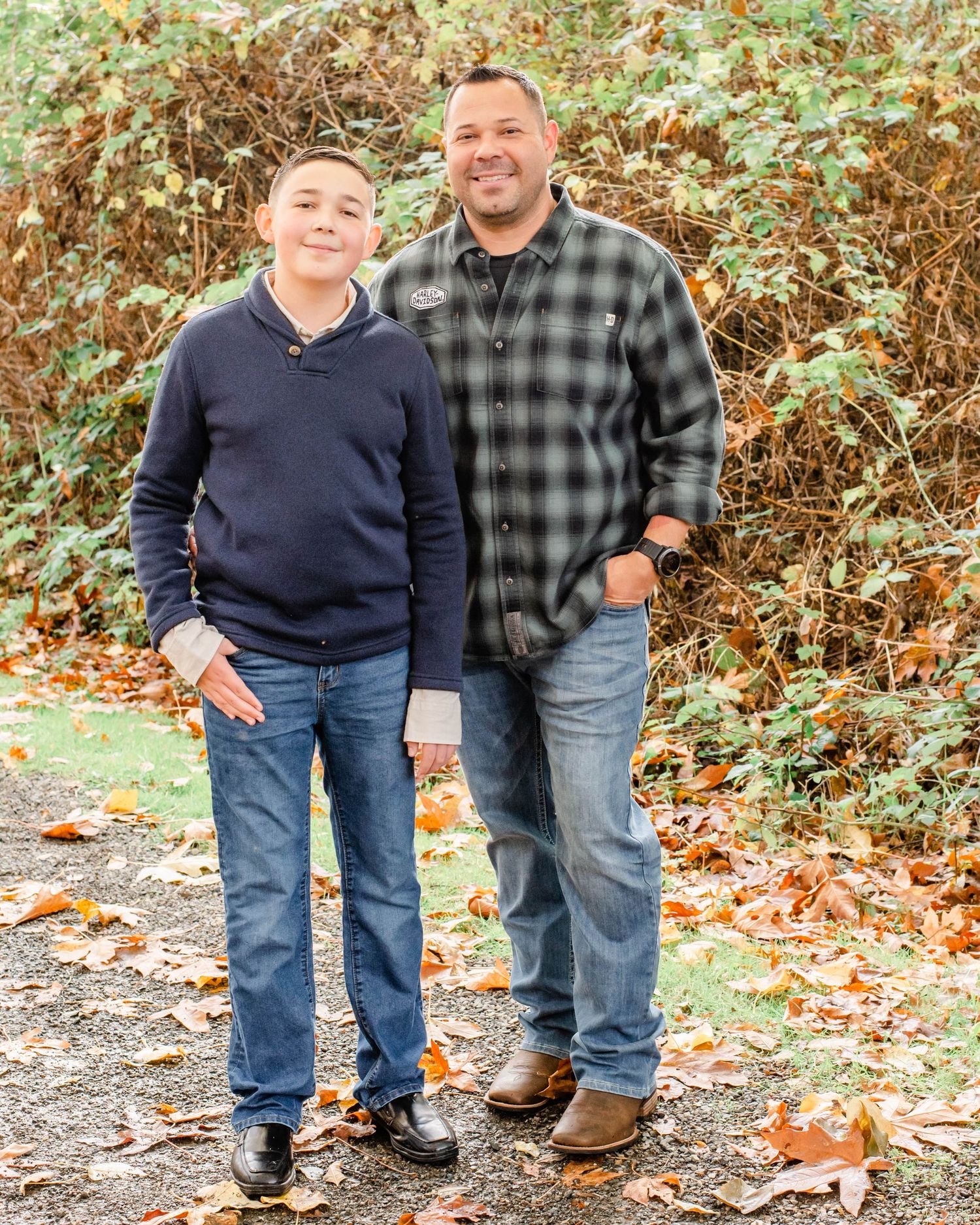 Two people in matching navy and plaid outfits pose together on an autumn day with fallen leaves in the background.