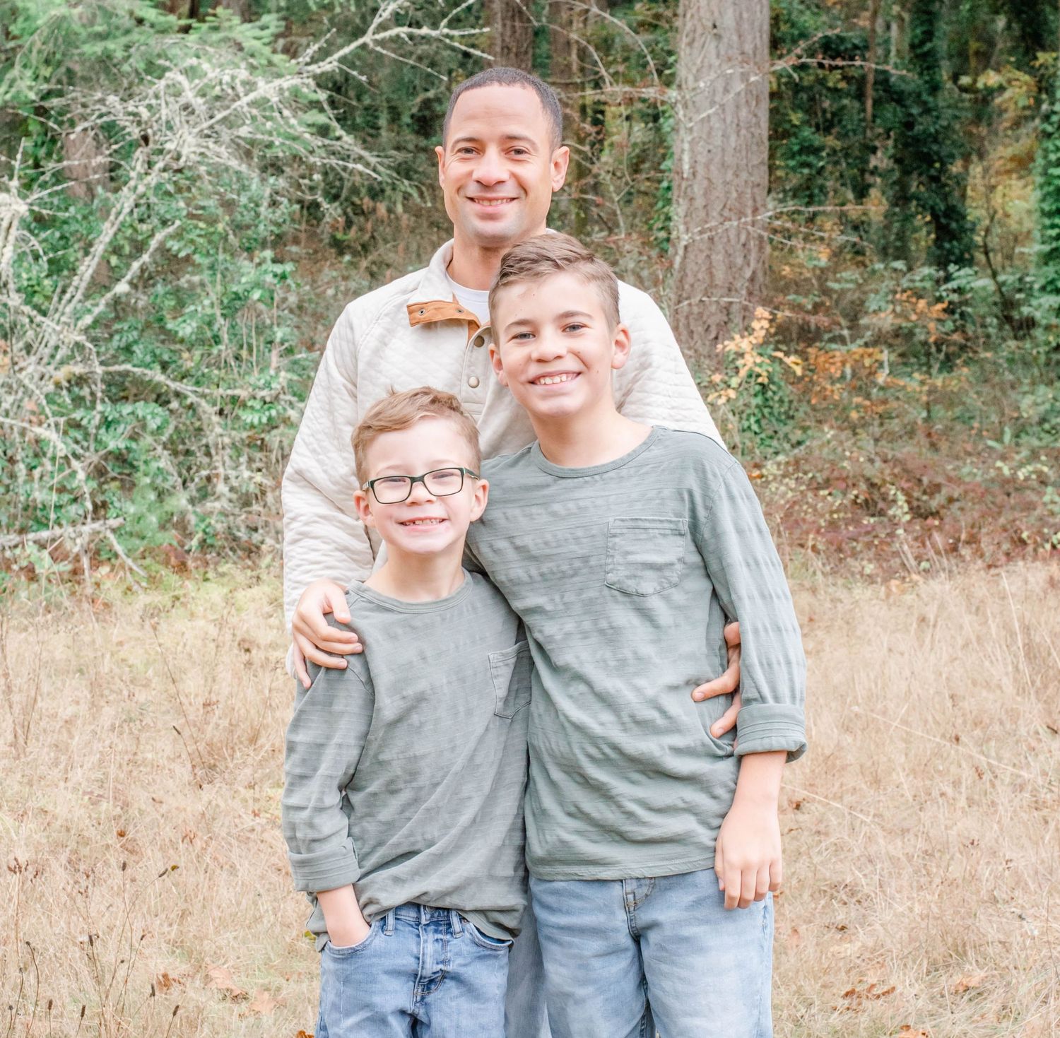 Siblings in matching gray shirts pose together in outdoor woodland setting.