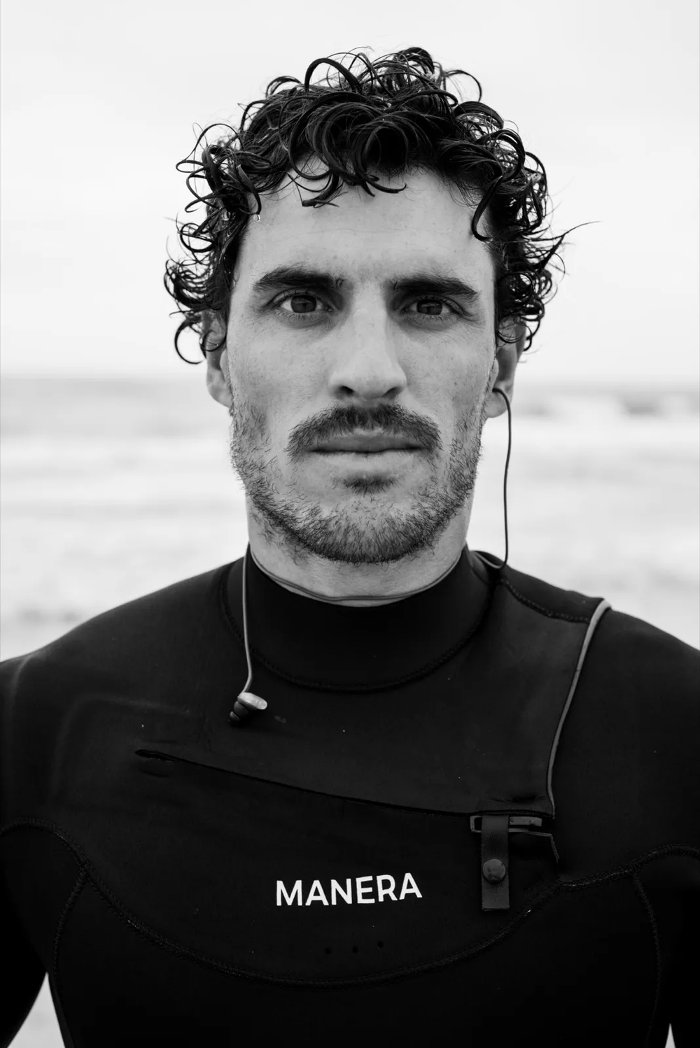 Portrait d’un homme en combinaison de surf, regard direct vers la caméra, fond minimaliste.