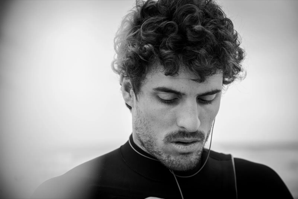 Portrait serré d’un surfeur les yeux baissés, visage mouillé et concentré, ambiance douce et contemplative.