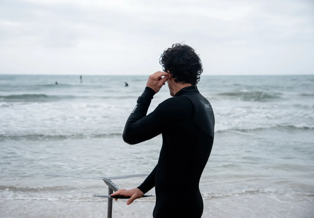Surfeur debout dans l’eau, tenant sa planche et regardant vers l’horizon.