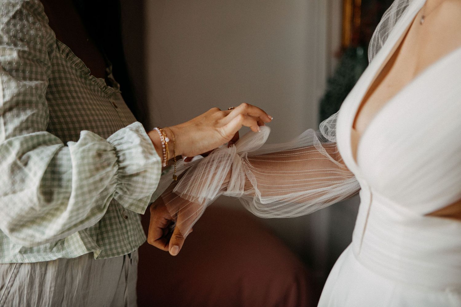 Close-up of hands adjusting the sheer tulle sleeve of a bride's white wedding gown.