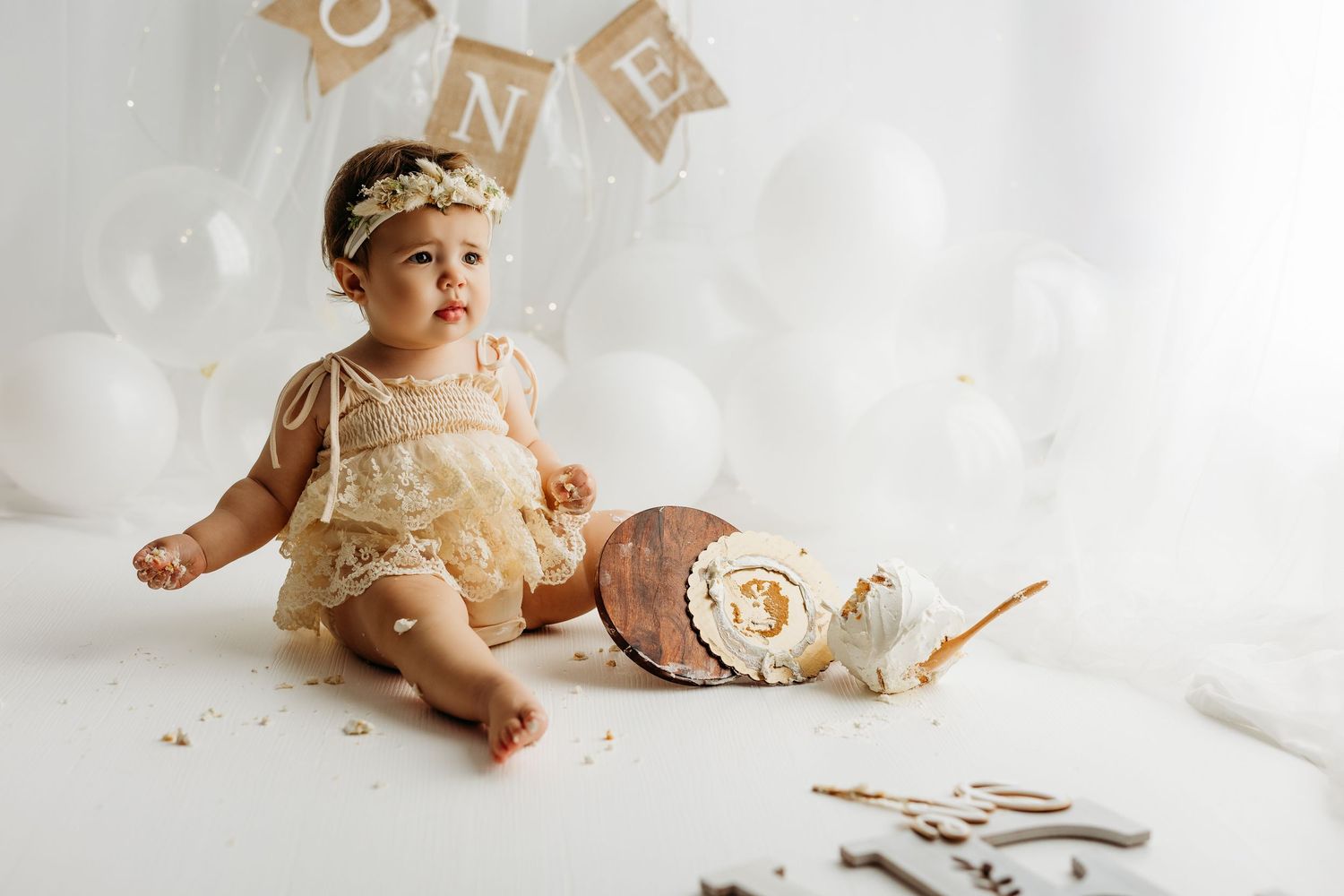 Baby in a cream lace dress crouches low on white background in professional studio portrait.
