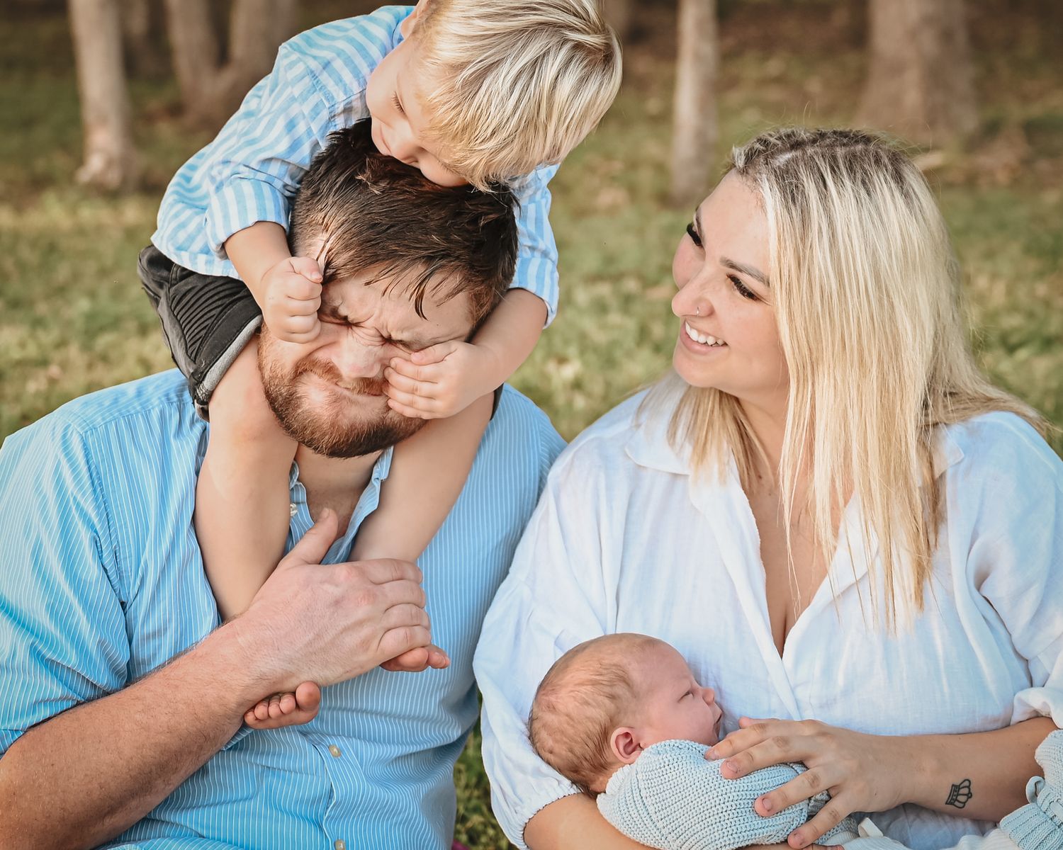 Outdoor family portrait in casual blue and white attire sitting together on a sunny day.