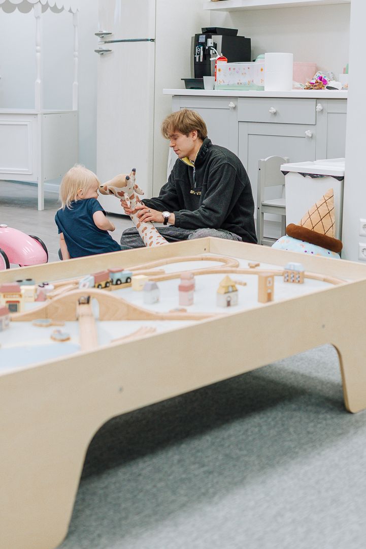 A pediatric dental exam room with a child patient next to a large wooden train play table.