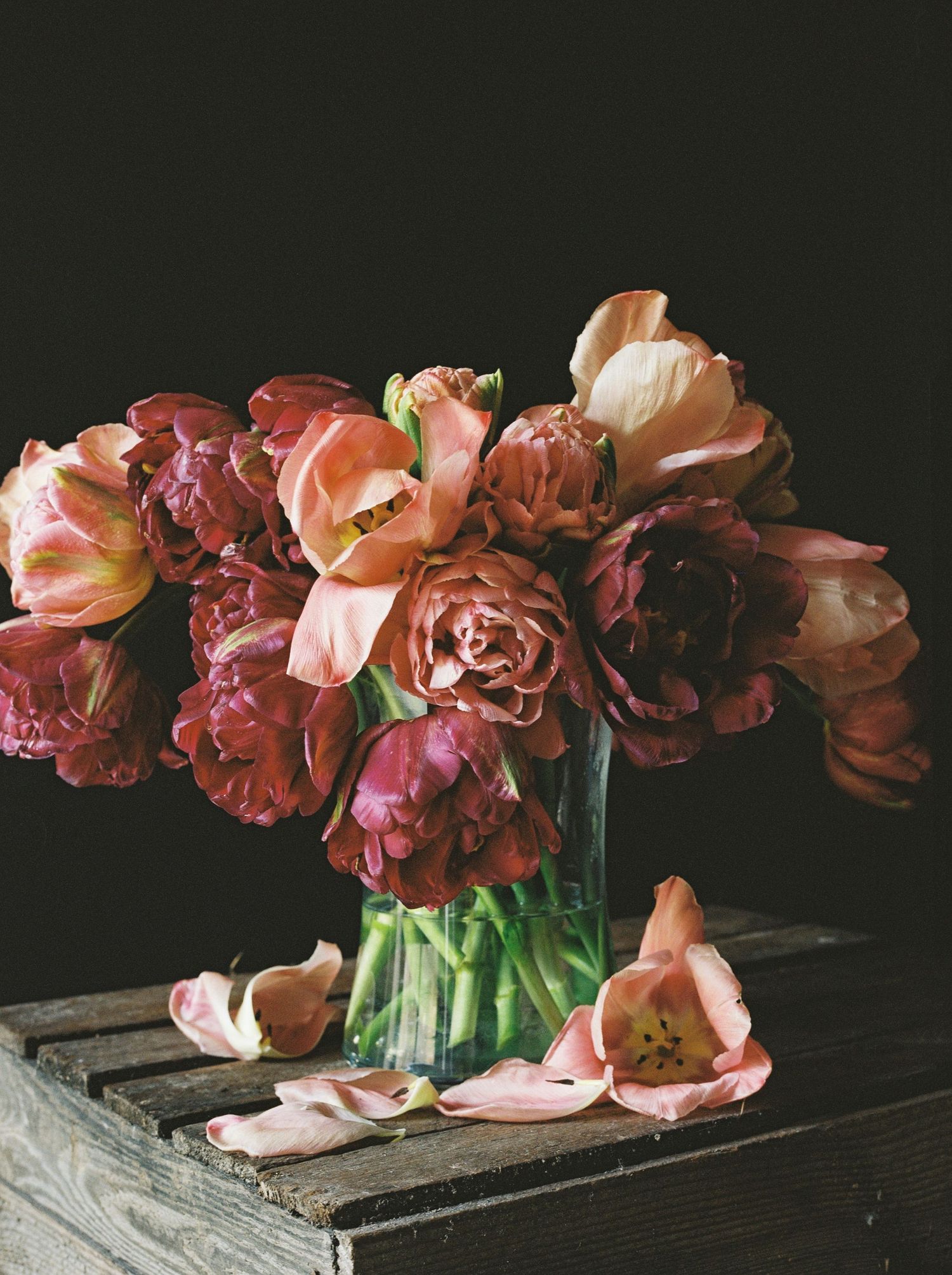 Still life of pink and burgundy tulips in a glass vase on weathered wood surface.