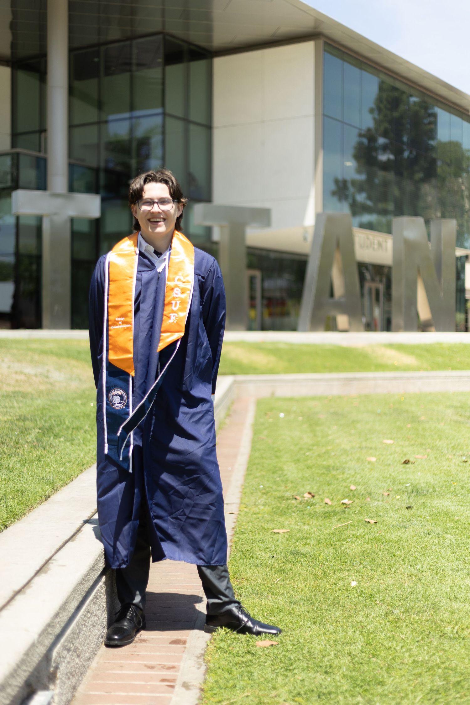 Grad student posing in front of Cal State Fullerton Titans sculpture.