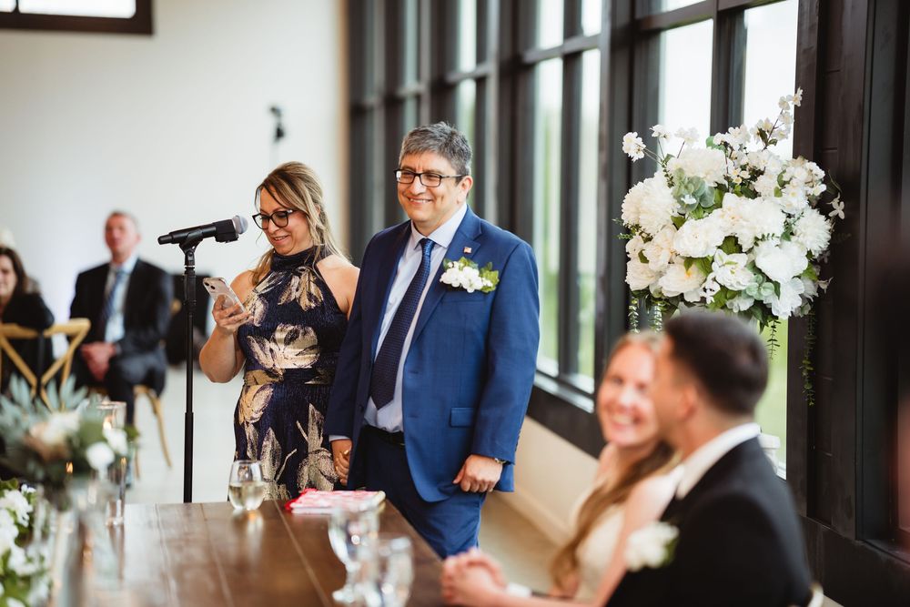 People delivering touching wedding reception speeches at an elegant venue decorated with white floral centerpieces.