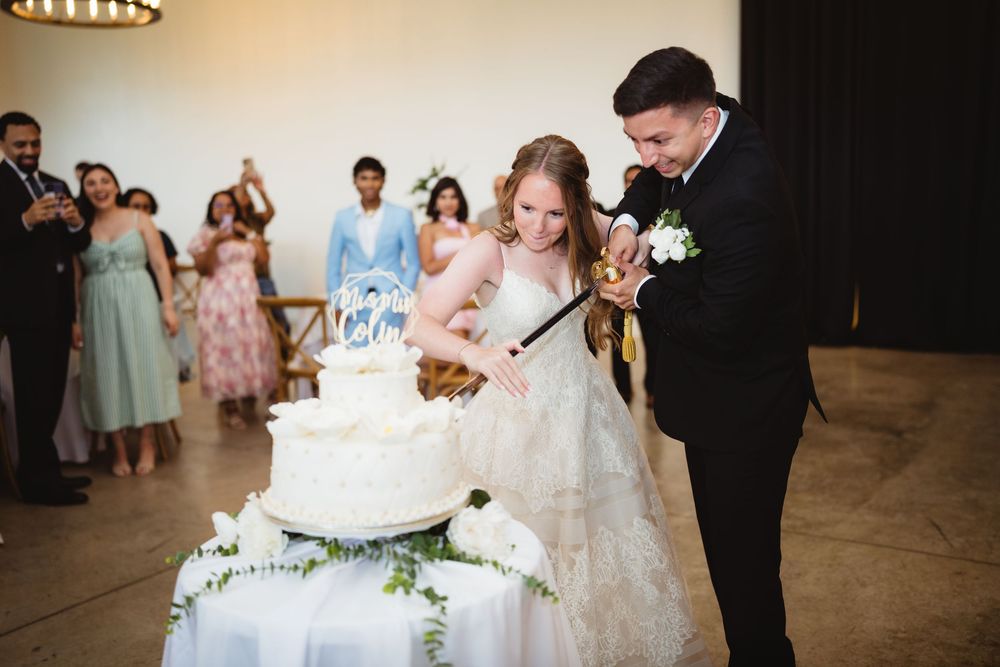 Newlyweds cut into their elegant white wedding cake adorned with flowers during their reception celebration.