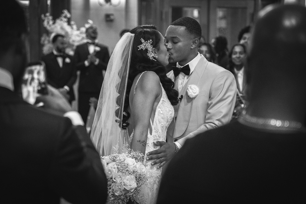 A romantic black and white wedding photograph capturing a tender kiss between newlyweds during their ceremony.