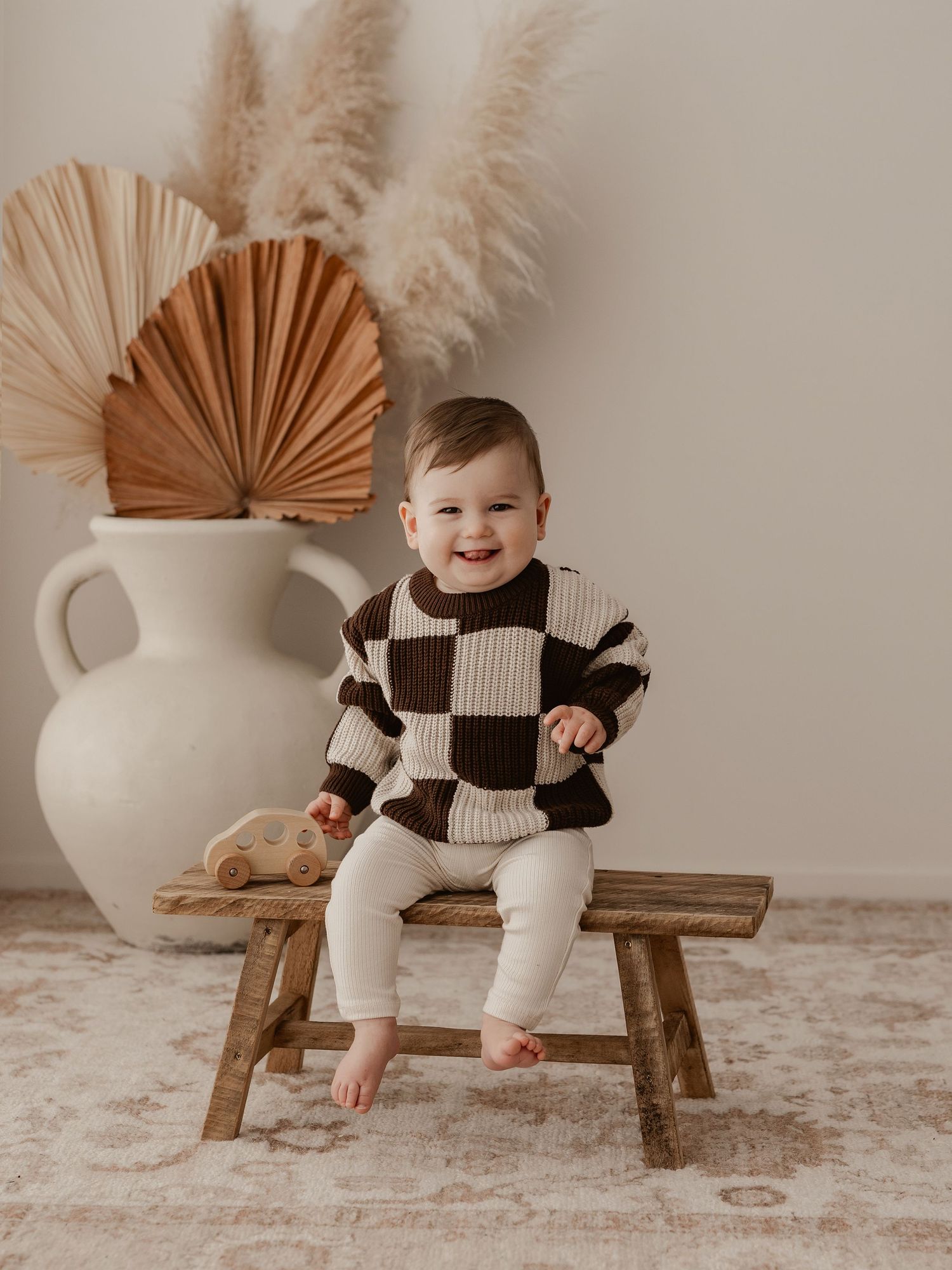 Two small children sitting together in matching beige outfits on wooden chair with rustic decor.