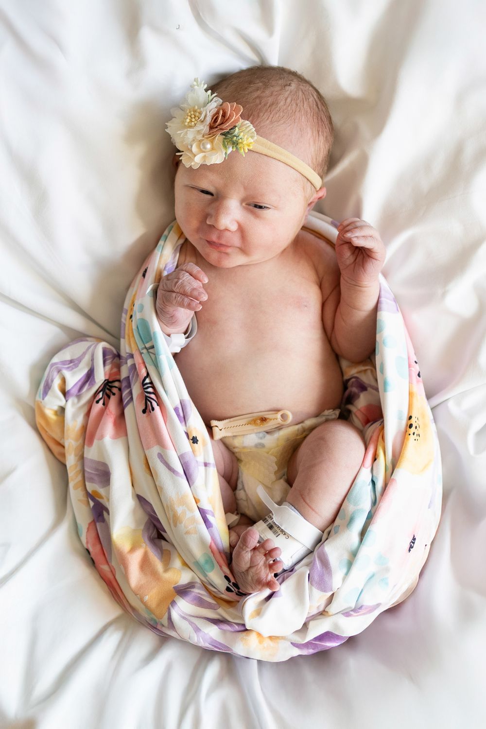 Newborn wrapped in soft floral swaddle blanket wearing delicate flower headband on white background. Detail shot. Newborn Pose.