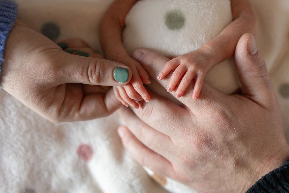 Close-up of newborn baby tiny fingers held gently by two adult hands on a soft polka dot blanket.