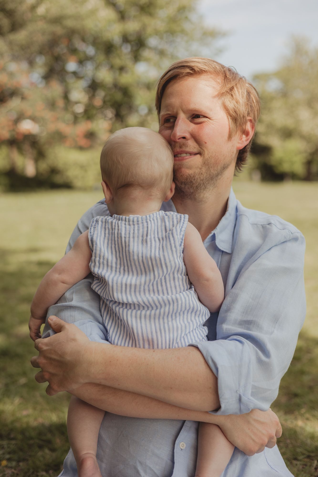 a father (dad) holds his baby to his chest on a sunny day in an outdoor park