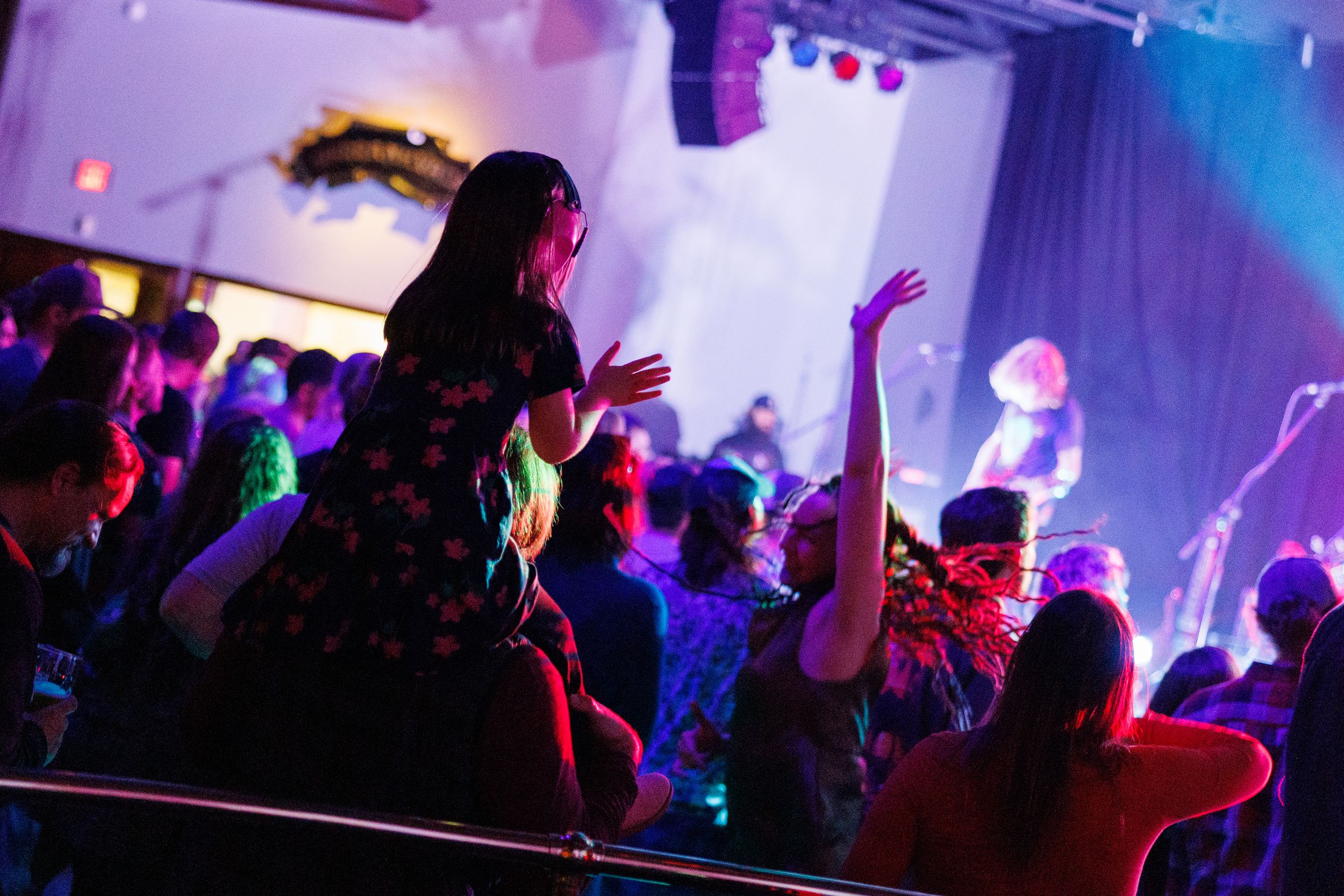 A lively nightclub scene with silhouettes of people dancing and partying under colorful purple and blue lighting.