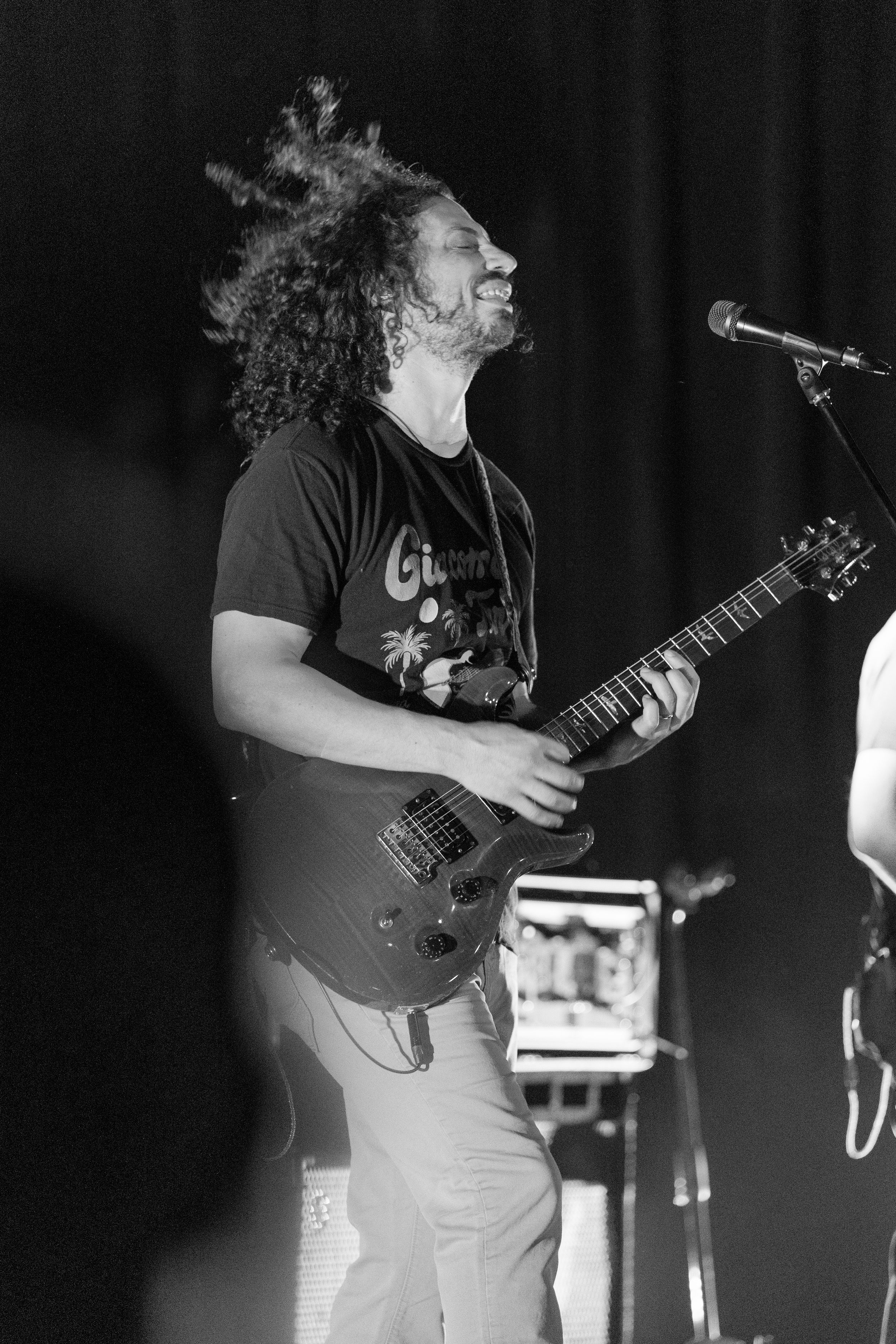 A guitarist in a black t-shirt performs on stage with a guitar, captured in black and white photography.