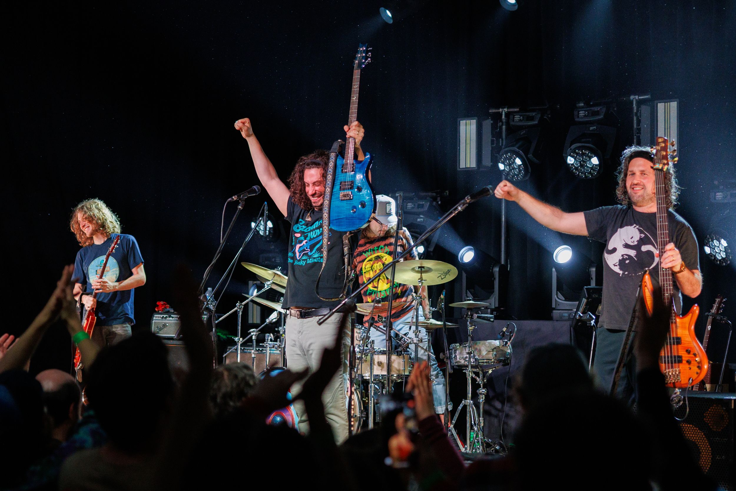 Rock band performs energetically on stage with musicians jumping and playing instruments during live concert performance.