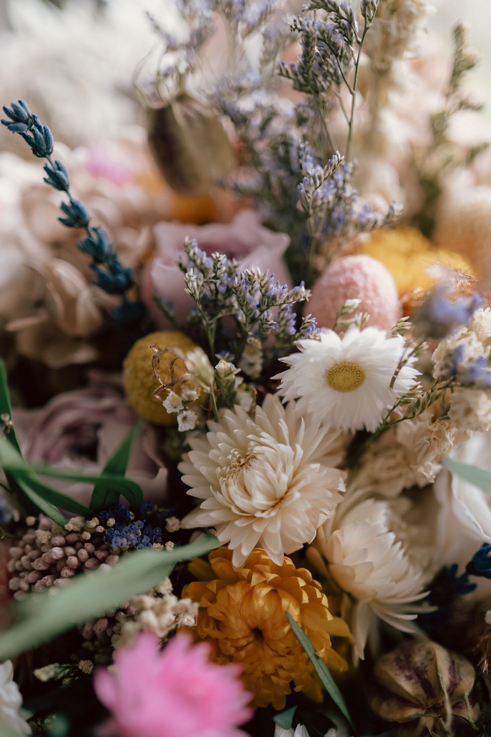 Close-up of a lush dried flower bouquet featuring white daisies, pink roses, lavender, and golden blooms in soft pastel tones.
