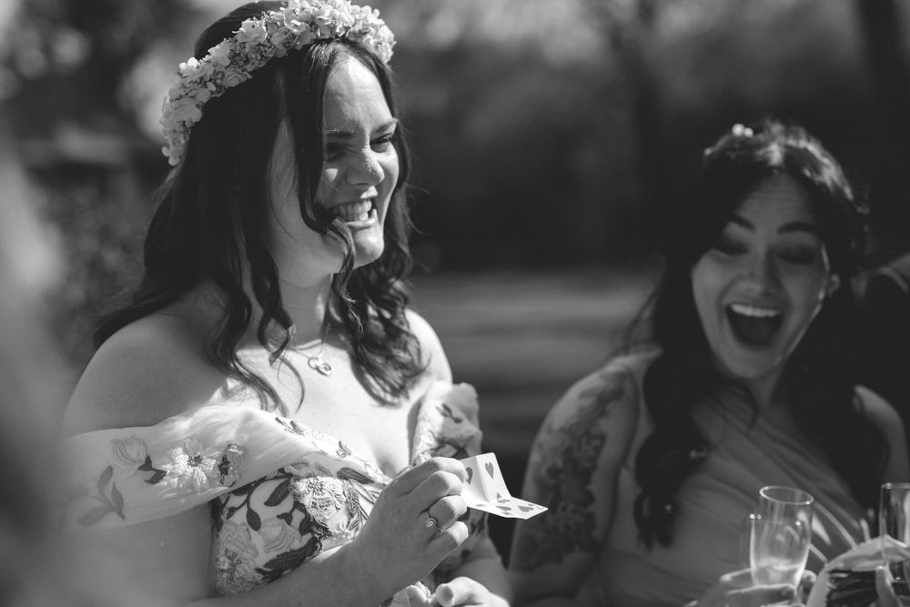 Candid Black and white photo of a laughing bride wearing a floral crown at an outdoor wedding reception.