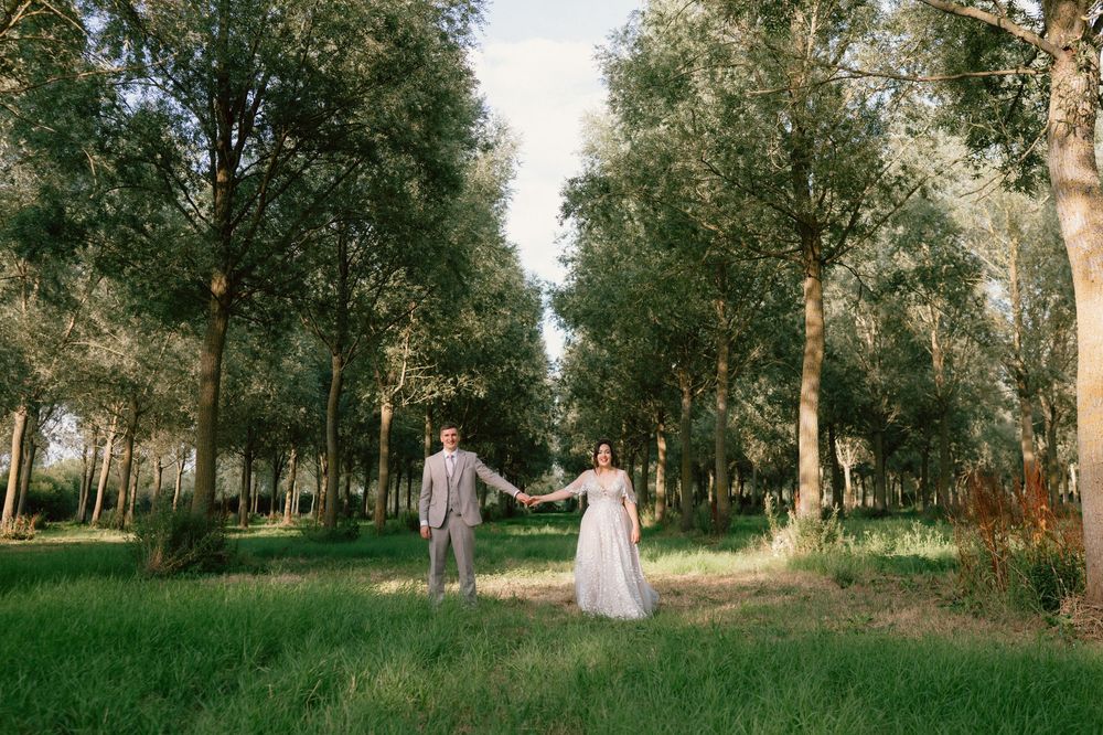 A bride and groom hold hands in a lush green tree-lined path on their wedding day at castle barn in Leicestershire
