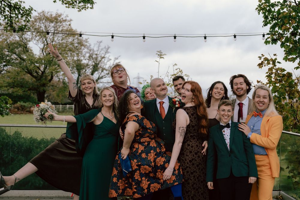 Group of joyful diverse LGBTQ+ wedding guests posing together outdoors under festoon lights at a wedding celebration at Llechwen hall hotel