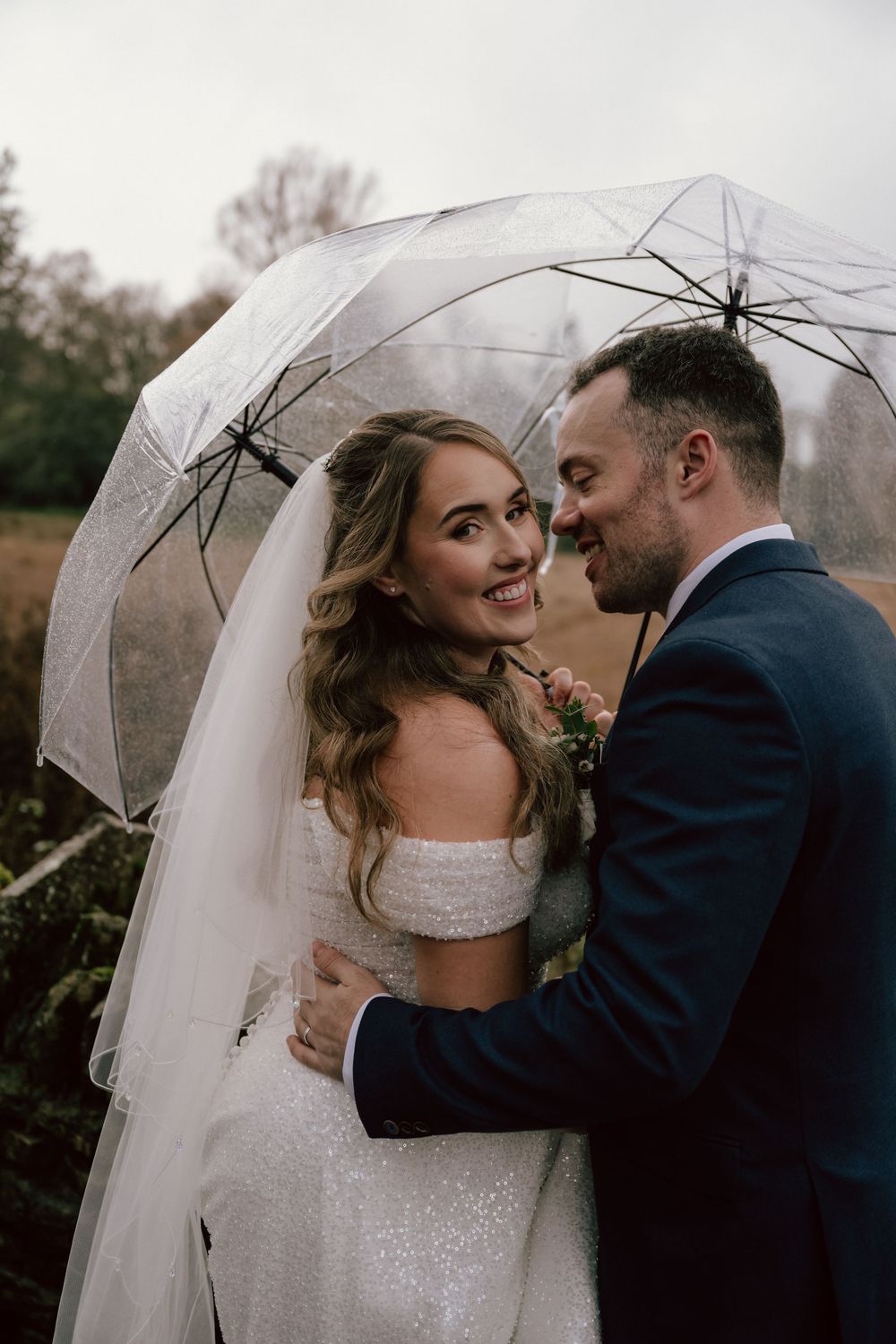 Bride and groom share a romantic moment under a clear umbrella on their rainy wedding day outdoors in Arlington row, Bibury in the Cotswolds