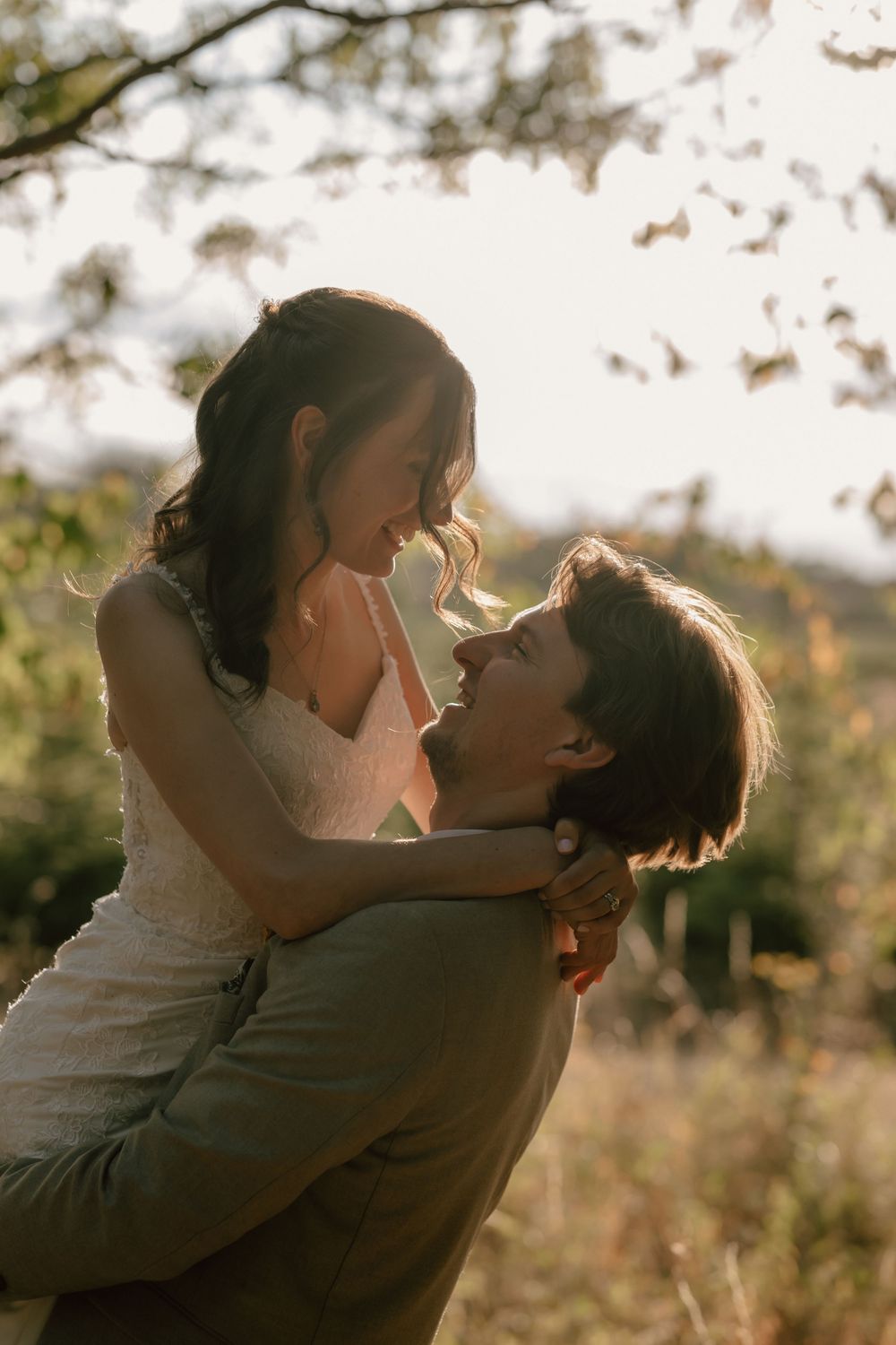 Couple sharing a romantic embrace outdoors in golden sunlight, man lifting woman among autumn trees.