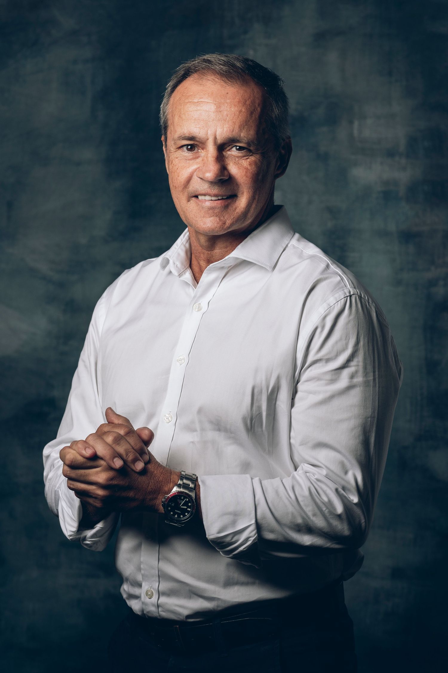 Professional headshot of a person in a white dress shirt against a textured backdrop.