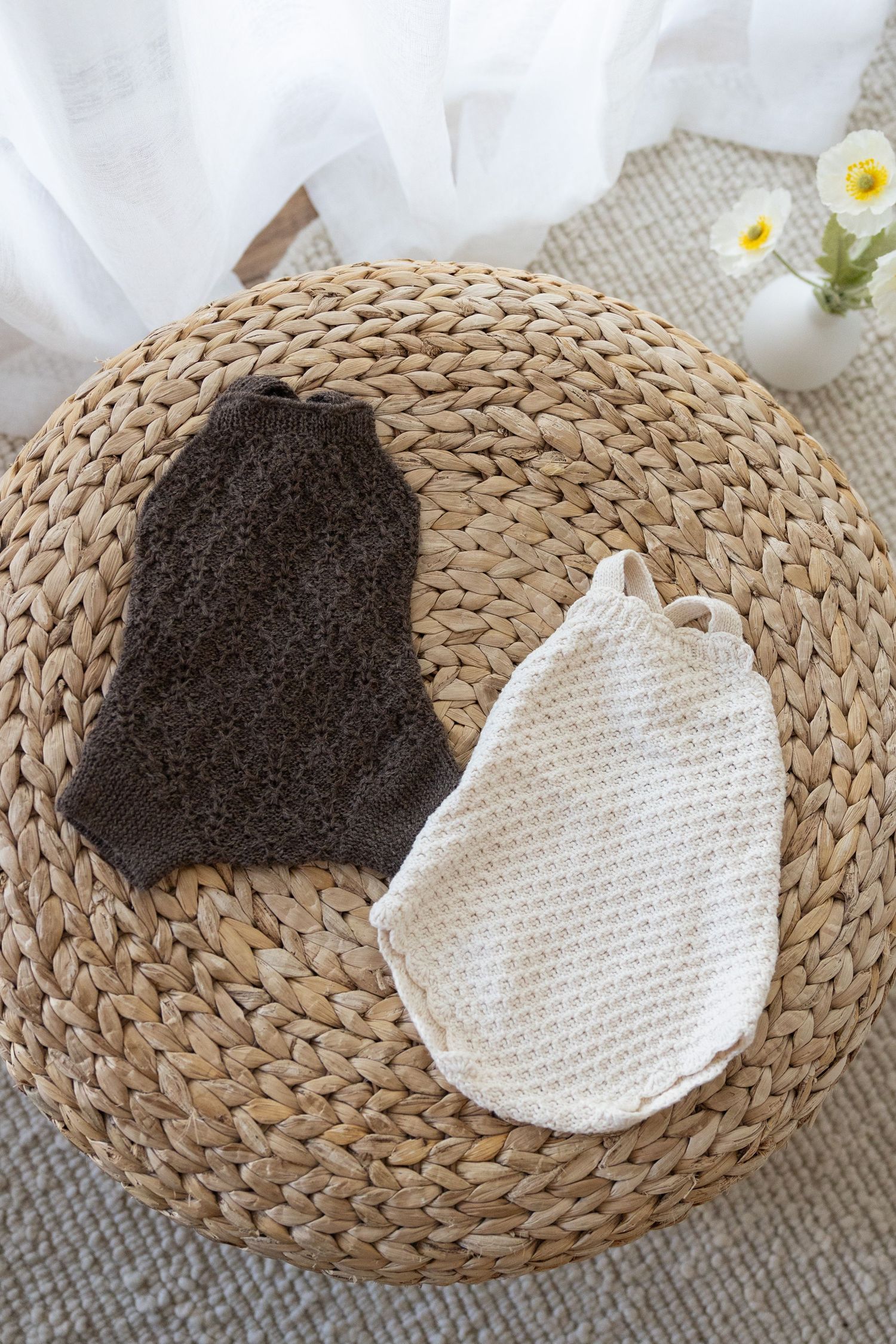 Natural brown loofah sponge and white cotton washcloth displayed on woven rattan placemat with small flowers in background.