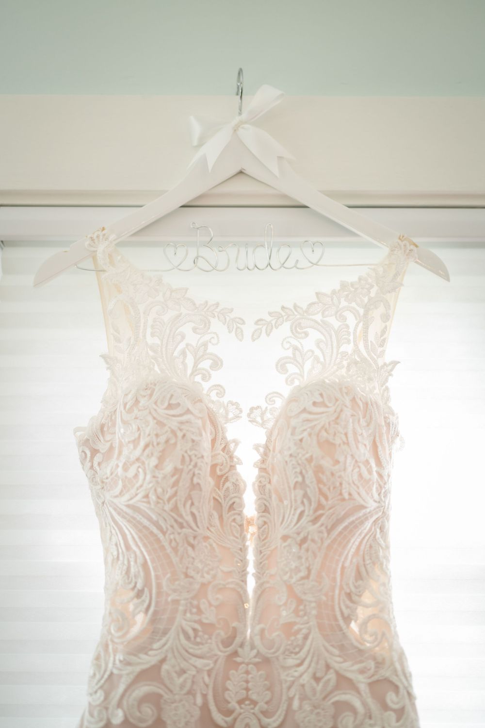 Close-up detail of an intricate lace wedding dress bodice hanging on a personalized white hanger.