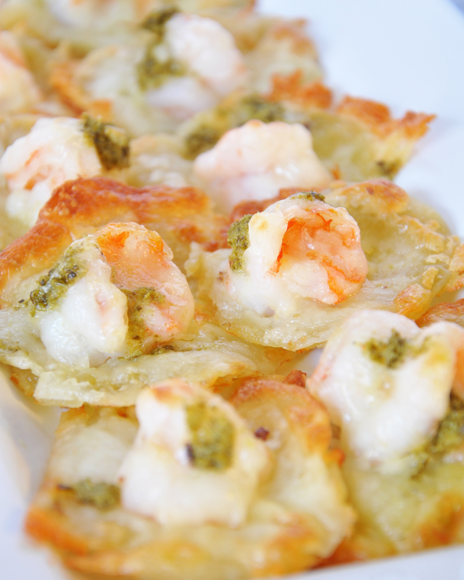 Close-up of shrimp and pesto on a white circular appetizer.