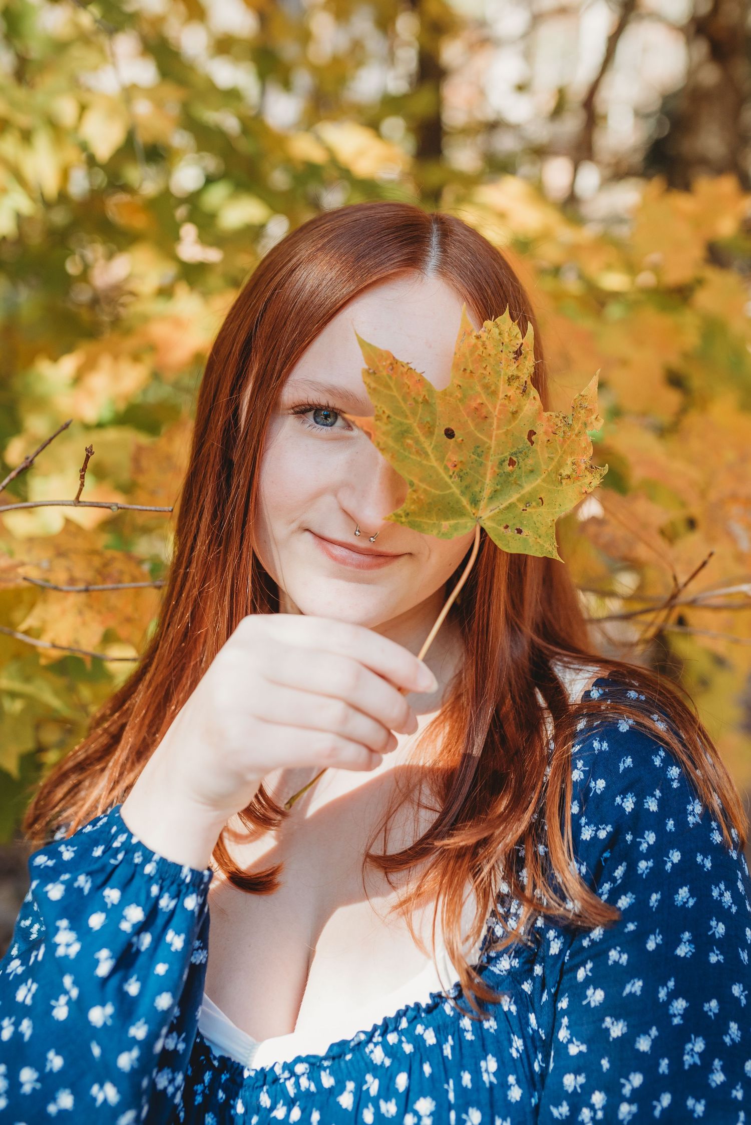 Playful fall portrait holding a yellow maple leaf against autumn foliage.