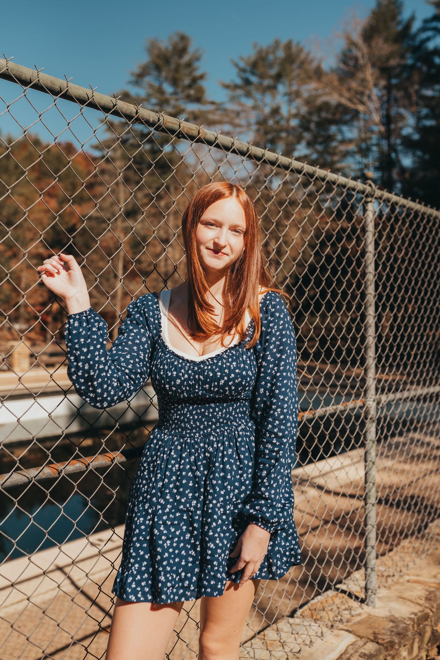 A cheerful pose by a chain link fence on a sunny autumn day.