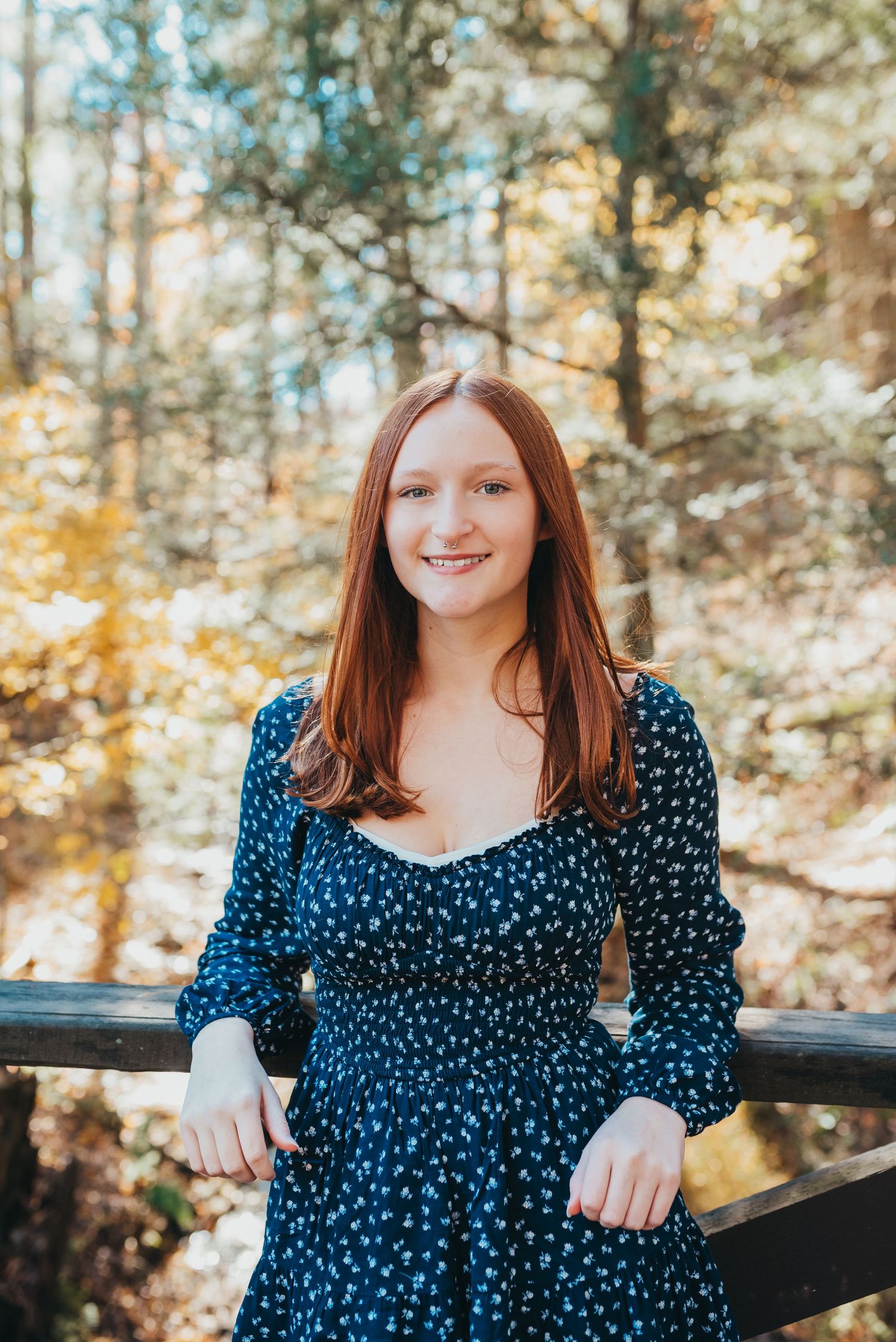 A bright portrait against rustic wooden rails with autumn trees in the background.