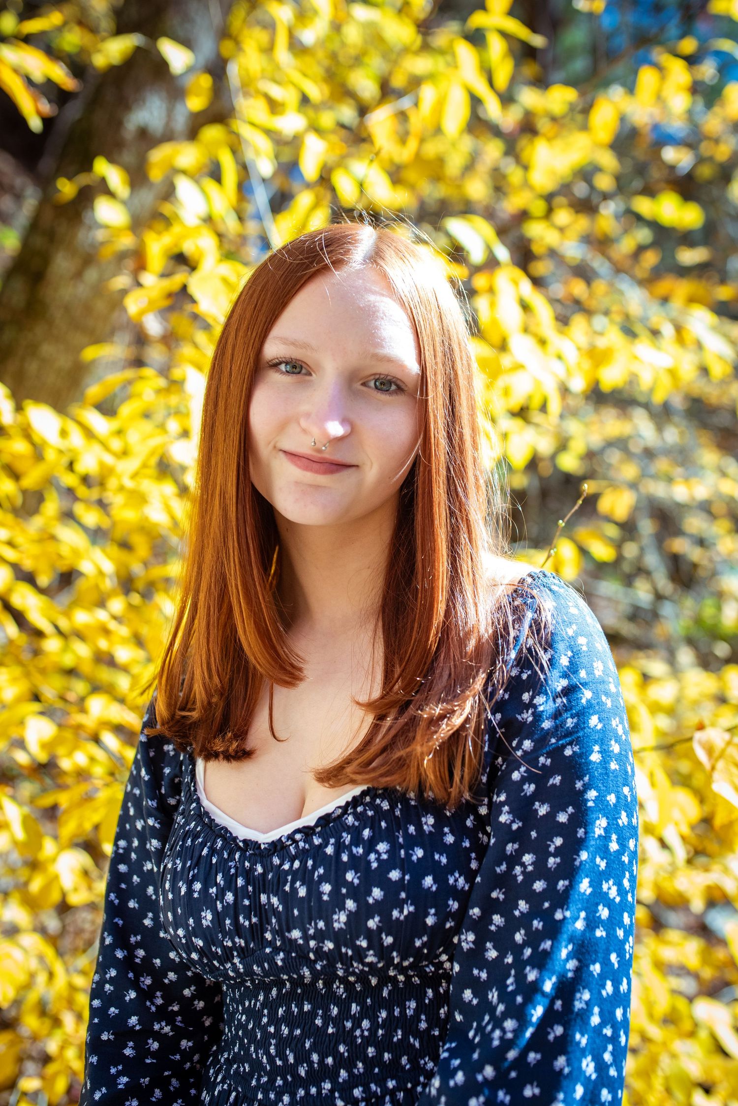 A portrait against vibrant yellow autumn foliage wearing a navy polka dot dress.