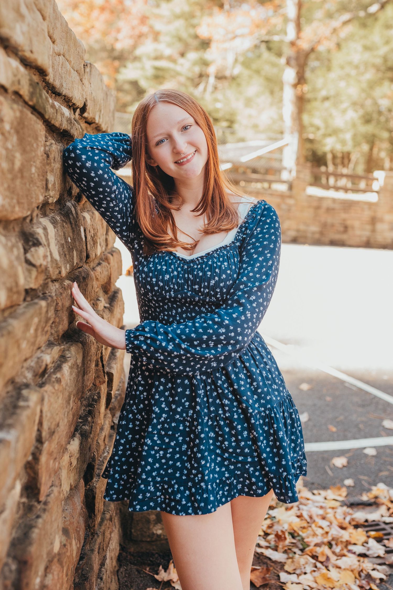 A casual portrait leaning against a stone wall in a blue patterned dress.