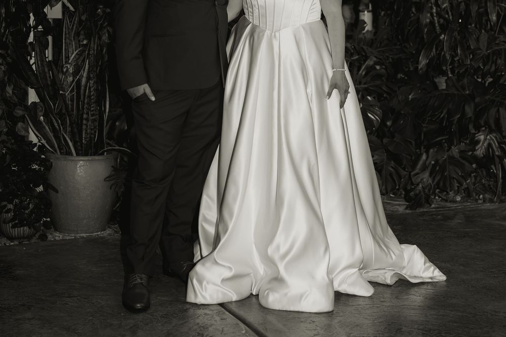 Black and white photo showing the elegant drape of a wedding dress next to formal shoes.