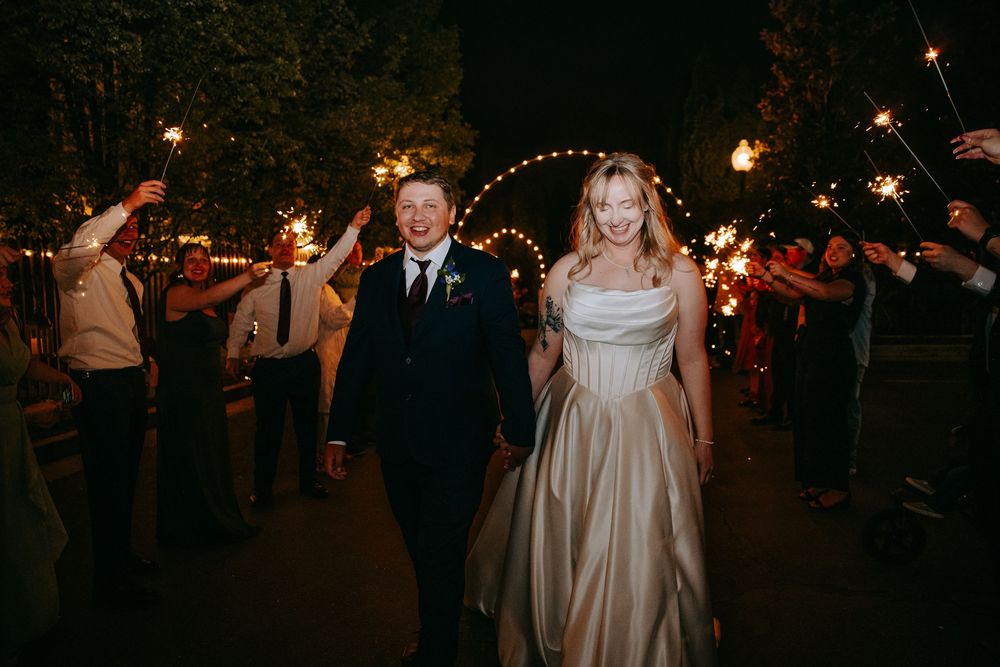 Couple walking through sparkler send-off line at nighttime wedding celebration.