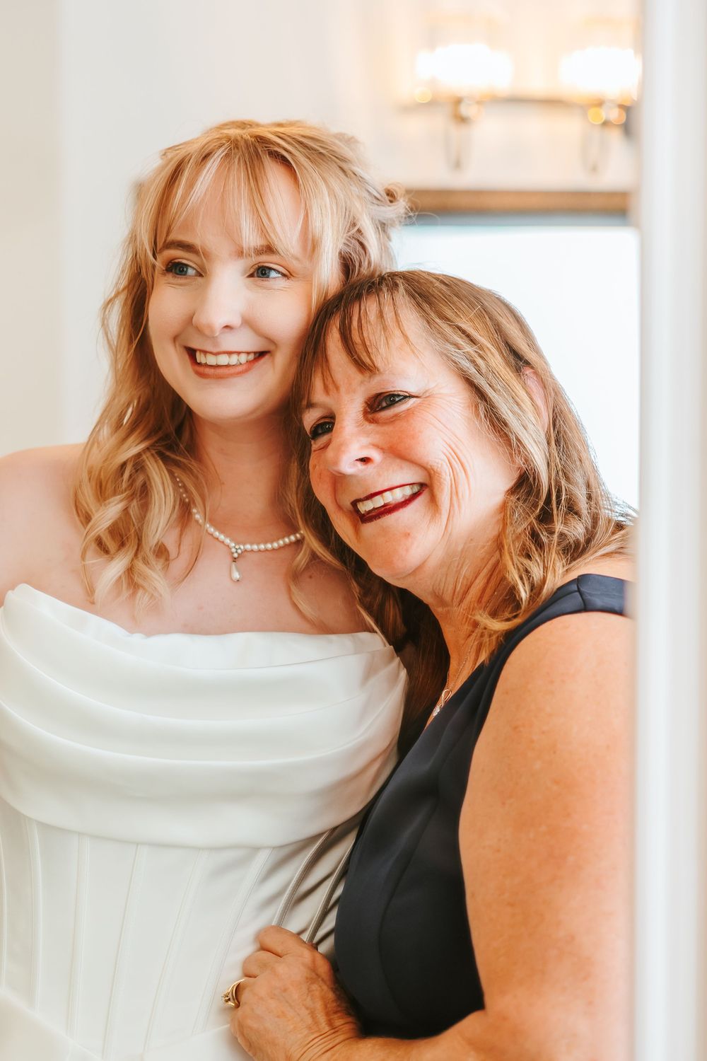 Sweet candid moment captured between two women in formal attire at wedding celebration.