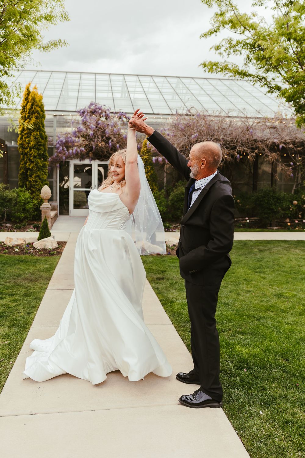 A joyful wedding moment with a dancing couple in front of a greenhouse with cherry blossoms blooming.
